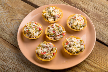 Salad in tartlets with shrimps and pineapple on a plate on a wooden table.