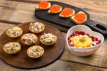 Toasts with red trout and butter and salad in tartlets on a board on a wooden table.