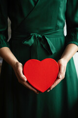 Woman in green dress holding a red heart gift box.
