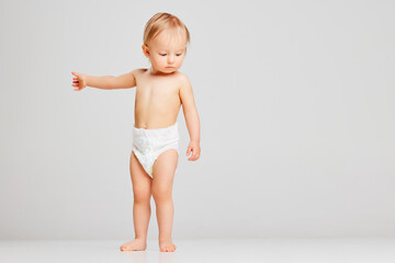 Little sad scared toddler girl, baby in diaper standing isolated on grey studio background. Concept...