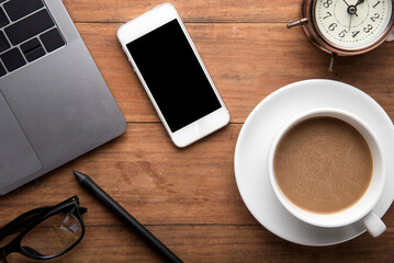 Smart phone, laptop computer, coffee cup and notebook on wooden background.