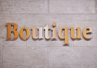 Golden 3D shiny boutique sign text on textured stone wall. Retail fashion shop and souvenir store concept.