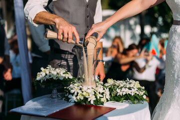The bride and groom are pouring sand together at a wedding ceremony at a hotel. On the table was a...