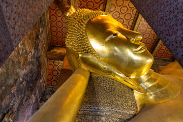 Golden face of long reclining Buddha statue at Wat Pho Temple in Bangkok, Thailand.