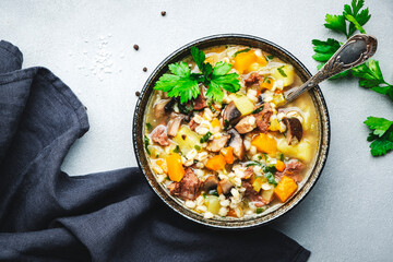 Winter comfort food. Warming high-calorie soup with pumpkin, mushrooms, potato, beef and barley. Gray table background, top view, copy space