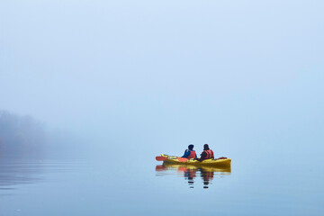 Back view of couple kayaking in a yellow tandem kayak in Danube river at misty autumn morning