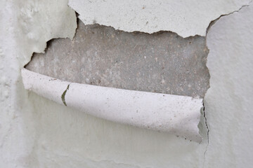 A layer of white paint peeling from a concrete wall due to effects of weather and damp conditions....