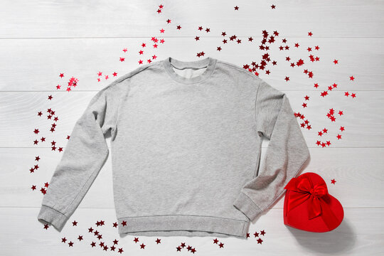 Grey sweatshirt mockup. Valentines Day concept shirt, giftbox heart shape on wooden background. Copy space, template blank front view clothes. Romantic outfit. Flat lay birthday holiday fashion