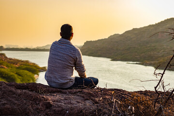 isolated young man sitting at mountain top with lake view from flat angle