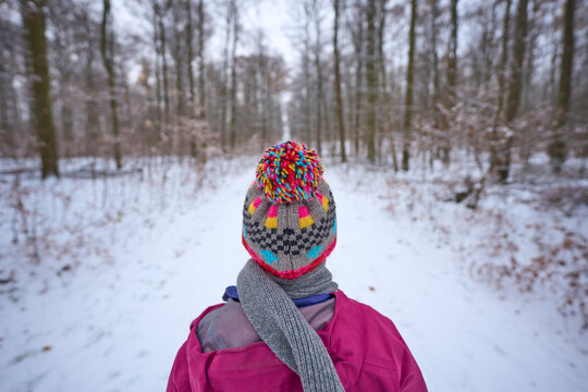 young woman with colorful wool hat hiking in a snowy winter forest
