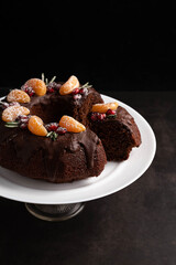 Blurred image of a chocolate cupcake decorated with tangerine slices, pomegranate berries, rosemary sprigs on a dark background.