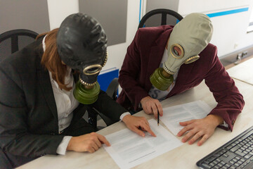 Man and woman working on a computer in the office, businesspeople in a suit with gas mask against...