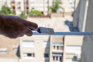 Hand holding a brush while painting a metal element of a window jalousie