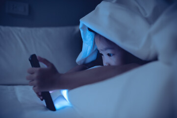 Obraz na płótnie Canvas Asian kid playing game on smartphone in the bed at night,The girl Addict social media