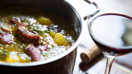 Pot with cooked octopus stewed with potatoes and a glass of red wine on the side.
