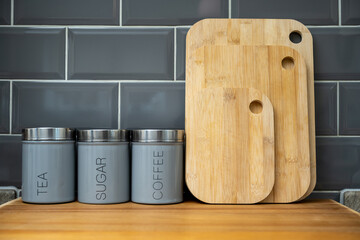 coffee tea and sugar air tight cannisters with bamboo chopping boards in the kitchen against a grey tiled background