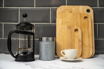 coffee air tight cannister Glass Cafetiere with coffee cup and saucer bamboo chopping boards in the kitchen against a grey tiled background