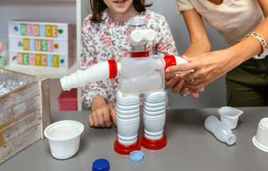Unrecognizable student and teacher making recycled toy robot with plastic packages in ecology...