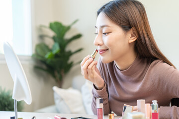 Skin care cosmetics concept, hand of woman, girl make up face by applying red lipstick, lips balm on her mouth, looking at the mirror at home. Female look with natural fashion style.