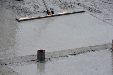 A building worker bull-floating the wet concrete,  a plumbing and water installation