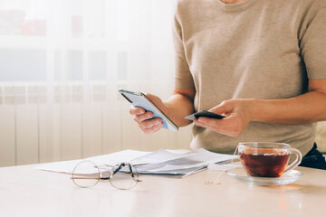 Woman holds phone in her hands for paying bills, receipts of financial checks, budget planning