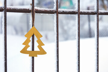 A Christmas tree toy made of plywood on a metal fence in frost. In the background , a country house...