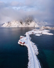 Aerial: Traditional scandinavian red cabins called rorbue under the winter fresh snow on fjord in front of the mountain
