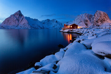Night landscape: traditional Scandinavian red house called rorbue standing alone on the fjord. Norway, Lofoten islands
