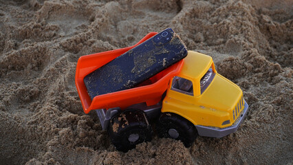A phone on top of a toy car on the beach