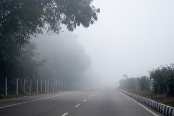 Early morning drives on empty road with trees bushes surrounding it with dense fog showing the cold chilly morning in Delhi, Rajasthan, Haryana India