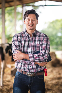 Asian man holding digital tablet for working in dairy farm, New generation agricultural farmer using technology for manage in small business smart farm, Livestock and farm industry.