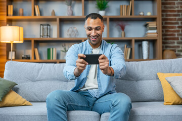 Young asian man sitting on sofa and playing games on phone at home