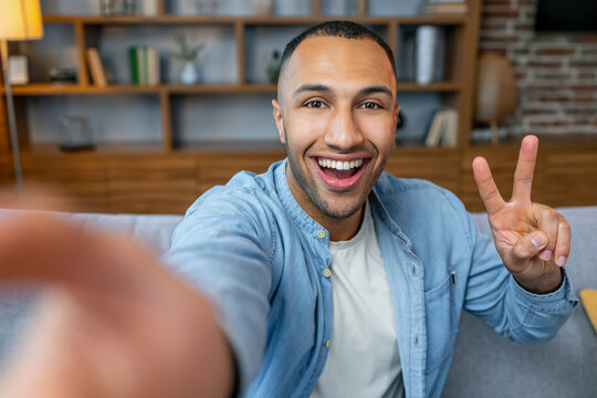 Close Up Young Smiling Happy Man In Casual Clothes Doing Selfie Shot Pov On Mobile Phone Sitting On Blue Sofa At Home Flat Indoors Rest Relax On Weekends Free Time. People Lounge Lifestyle Concept.