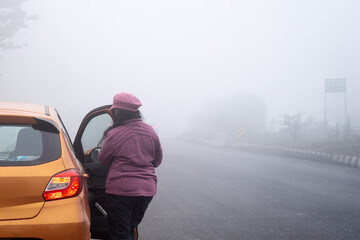 Young indian female in pink clothes and hat with orange car preparing for long drive in the dense...