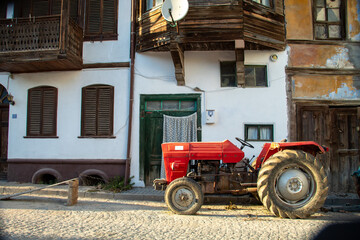 A red tractor in front of yellow and white coloured village houses