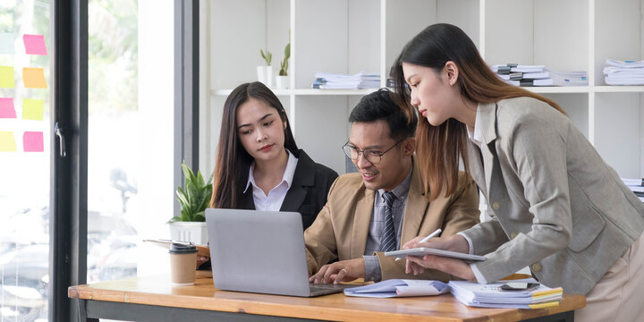 Group of young asian business people in smart casual wear working together in creative office using laptop.