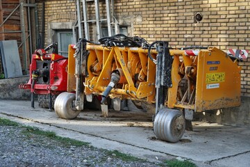 Yellow agriculture soil spading machine for tillage parked near the brick wall of farm building.