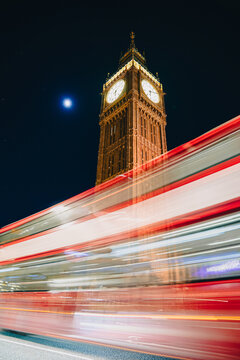 Travel to London. Landmark photo with the iconic Big Ben building after renovation and a double decker bus crossing in front of it with long exposure under the moonlight. Nigh photo in London.