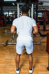 Fototapeta na wymiar Back side of a gym athlete wearing a white blank shirt pulling the cable rope at a gym