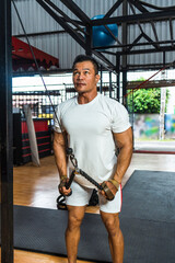 A gym athlete wearing a white blank shirt pulling the cable rope at a gym