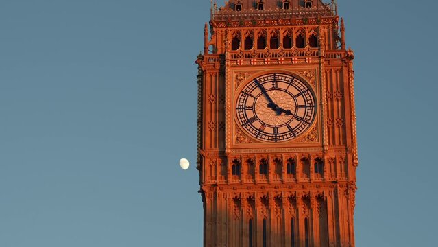 Travel to England, landmark 4k video. Big Ben tower clock building after renovation during a beautiful sunset with moon rising in background against clear sky.
