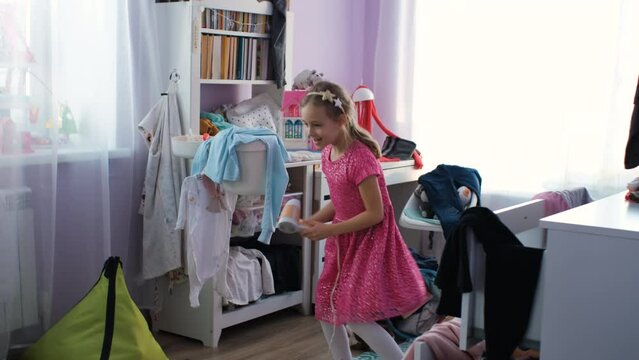 Happy little girl singing in hairdryer at home, having fun and dancing in messy room, slow motion