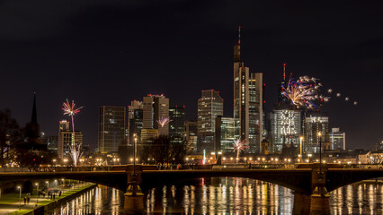 Plakat New years eve with fireworks above the skyline of Frankfurt - Main at night at a cold day in winter with colorful reflections in the water.