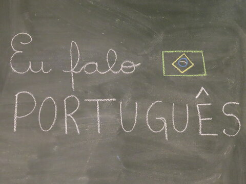 Frase EU FALO PORTUGUÊS escrita com giz de lousa em quadro escolar verde e desenho da bandeira do Brasil 