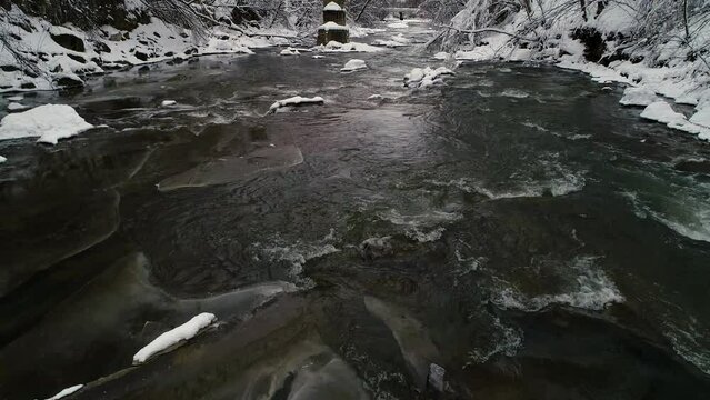 Flying over a fast flowing mountain winter river on a cloudy day. Winter landscape.
