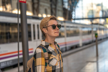 Adult 35s year old lesbian woman in plain shirt and jeans with backpack and sunglasses traveling by train in Europe. Train station in Barcelona, Spain.