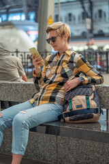 Fototapeta premium Adult 35s year old lesbian woman in plain shirt and jeans with backpack and sunglasses traveling by train in Europe. Train station in Barcelona, Spain.