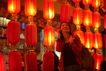 Woman talking on mobile phone with red lanterns in the background at night.