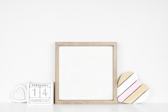 Mock up square wood frame with rustic Valentines Day wooden heart decor and calendar. White shelf against a white wall. Copy space.