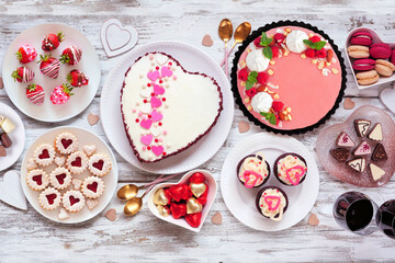 Valentines Day table scene with an assortment of desserts and sweets. Overhead view on a white wood...